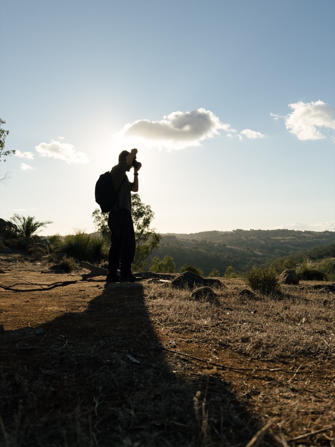 Silhouette of Carel with a camera and backpack on a hillside under a bright sky