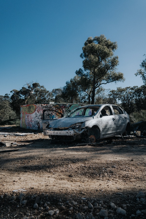 Weathered car among trees in sandy bushland